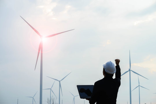 Successful engineer standing and hoding labtop with wind turbine.