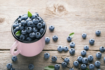 Ripe blueberries in pink mug on wooden table