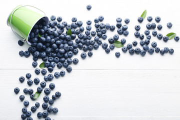 Ripe blueberries with green leafs on white wooden table