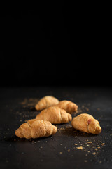 Fototapeta na wymiar several whole croissants with crumbs on a dark background