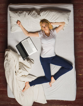 Woman Lying On Bed With Laptop. Overhead View.