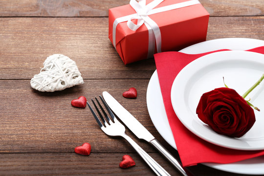 Kitchen cutlery with red rose in plate on wooden table