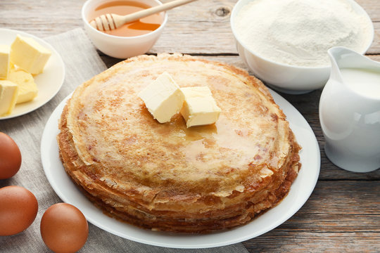 Heap of pancakes in plate with butter on grey wooden table