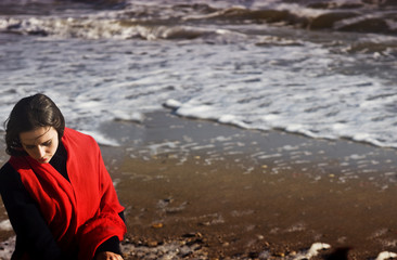 Girl with flying hair in a red kerchief looks at the sea waves on the beach