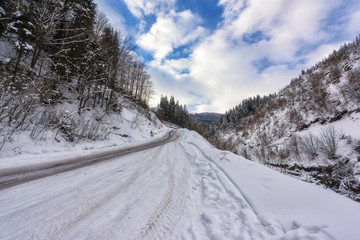 Fototapeta na wymiar Narrow winding mountain road in snow, daytime winter landscape with blue cloudy sky