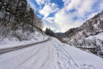 Obraz premium Narrow winding mountain road in snow, daytime winter landscape with blue cloudy sky