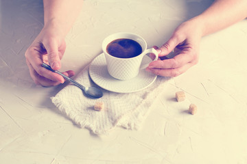 Coffee cup in female hands on a light, rough background