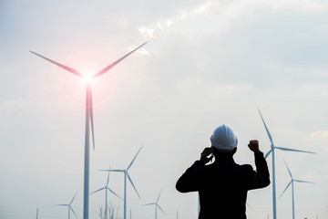 Successful engineer standing and hoding smartphone with wind turbine.