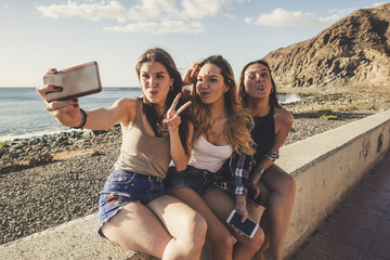 Three young woman using phone to take selfies in vacation near the beach