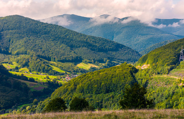 Naklejka premium village in the valley of Carpathian mountains. lovely countryside scenery in early autumn with clouds rising from the forest on the distant ridge