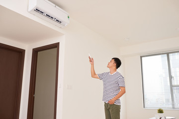 Fototapeta na wymiar Portrait Of Happy Man Using Remote Control To Operate Air Conditioner