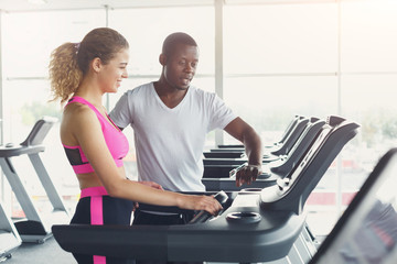 Fototapeta na wymiar Fitness instructor helps young woman on treadmill