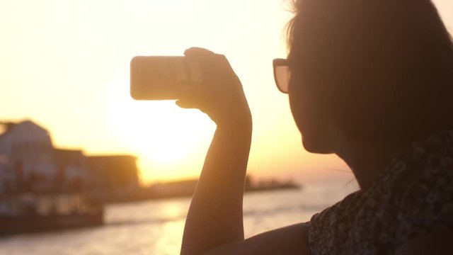 Young woman taking photo against impressive sunset during sea cruise with lens flare effects. Slow Motion. 3840x2160