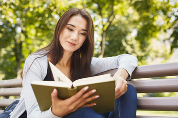 Fototapeta premium Young woman reading book in park copy space