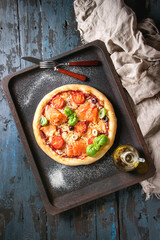 Traditional pizza with smoked salmon, cheese, tomatoes and basil served on old oven tray with textile and olive oil over dark blue wooden background. Top view with space. Rustic style