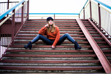 fashionable girl sits on the steps of the bridge