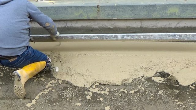 worker with an aluminum straightedge extends in a uniform manner the concrete to achieve a screed