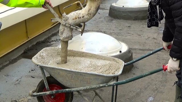 Worker loading wheelbarrow concrete from the pump concrete 