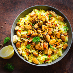 Traditional spanish seafood paella in pan rice, peas, shrimps, mussels, squid on light grey concrete background. Top view, copyspace. Square crop