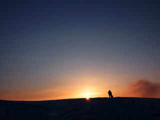 Naklejka na ściany i meble Silhouette of a man standing on snow mountain toward sunset 