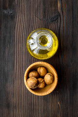 Oil as cosmetics. Walnut oil near walnut in nutshell on dark wooden background top view