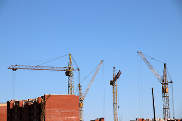 Old tower cranes raise brick blocks against a blue sky