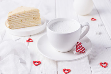 Happy Valentine's day. White cup with milk, homemade honey cake and red hearts on a white background