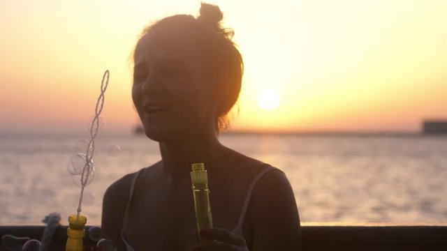 Happy brunette woman blowing soap bubbles on the cruise ship at beautiful sunset in the sea. Slow motion. 3840x2160