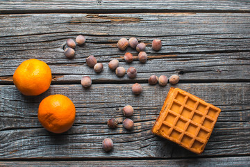 On wooden background are waffles, next to acorns and tangerines