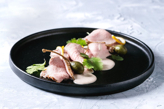 Vitello tonnato italian dish. Thin sliced veal with tuna sauce, capers and coriander served on black plate over gray texture background.