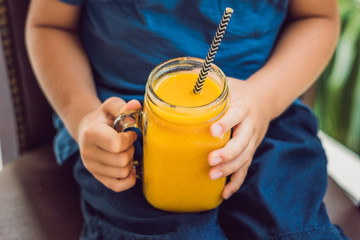 Boy drinking juicy smoothie from mango in glass mason jar with striped red straw on old wooden background. Healthy life concept, copy space © galitskaya