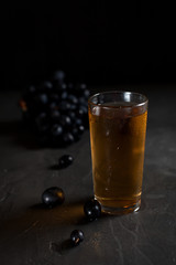 a glass of fresh grape juice and a bunch of juicy dark grapes on a dark background