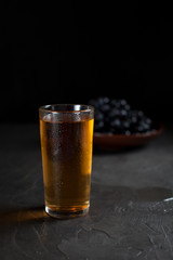 a glass of fresh grape juice and a bunch of juicy dark grapes on a dark background