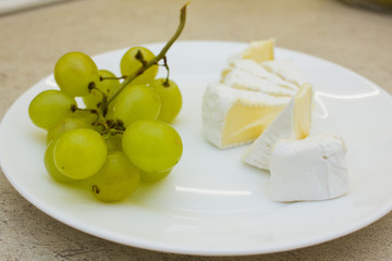 White plate with bunch of green grapes and cheese pieces on stone backgound