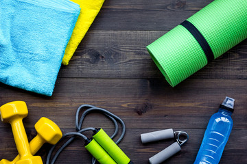 Fitness equipment. Jump rope, dumbbells, expander, mat, water on dark wooden background top view copyspace