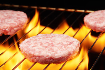 Raw hamburgers on grill with flame