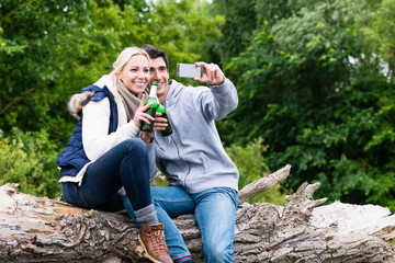 Woman and man drinking beer taking selfie while hiking in forest