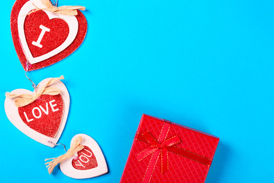 Valentine day concept. Inscription I love you on red decorative hearts with red gift box on blue background. Free space for your text.