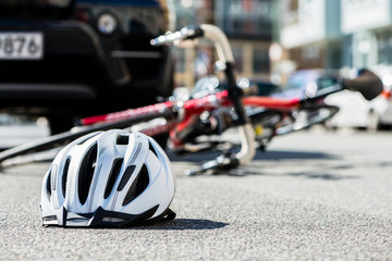 Close-up of a bicycling helmet fallen on the asphalt  next to a bicycle after car accident on the street in the city - obrazy, fototapety, plakaty