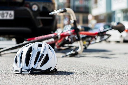 Close-up of a bicycling helmet fallen on the asphalt  next to a bicycle after car accident on the street in the city