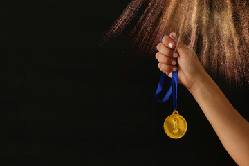 Fototapeta na wymiar Woman hand holding gold medal against black background with glitter overlay. Award and victory concept.