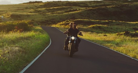 Couple riding vintage motorcycle on country road at sunset