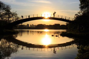Girl watching a colorful sunset by the lake, holding a heart-shaped balloon, at Ibirapuera Park, Sao Paulo, Brazil