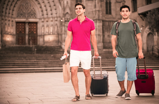 Men tourists are walking with suitcases in unknown city.