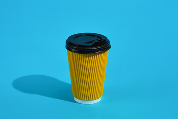 Hot coffee in yellow paper cup with black lid on blue background