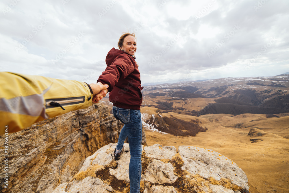 Wall mural happy young girl holding a guy by the hand, traveling through the caucasus mountains