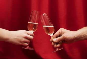 Hands Man and woman sitting at a table with glasses of champagne. red background