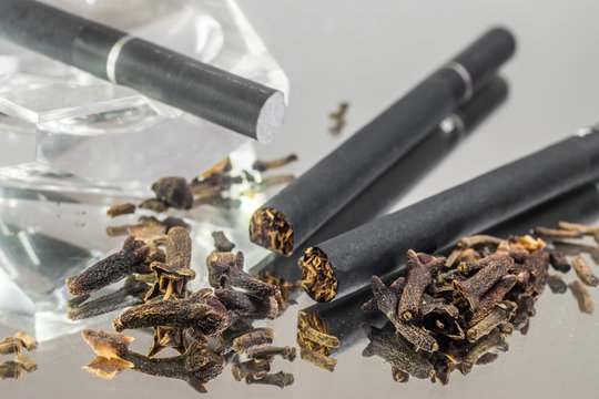 Kretek black clove cigarretes and cloves, with a transparent glass ashtray, on top of a mirror glass reflective surface