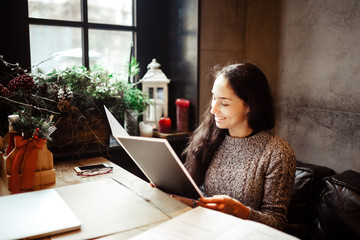 business girl studying the menu in restaurant decorated with Christmas decor.sits near the window...