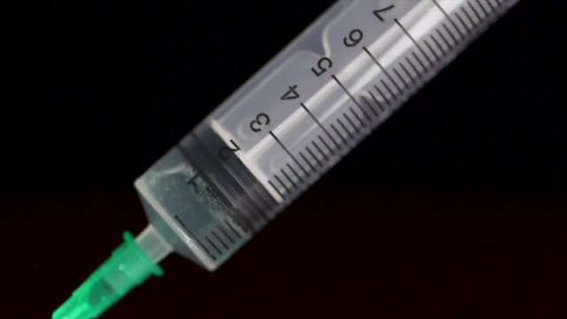 Hand holding a syringe, the syringe is filled with clear liquid is isolated on black background. Hypodermic syringe that is being filled with vaccine